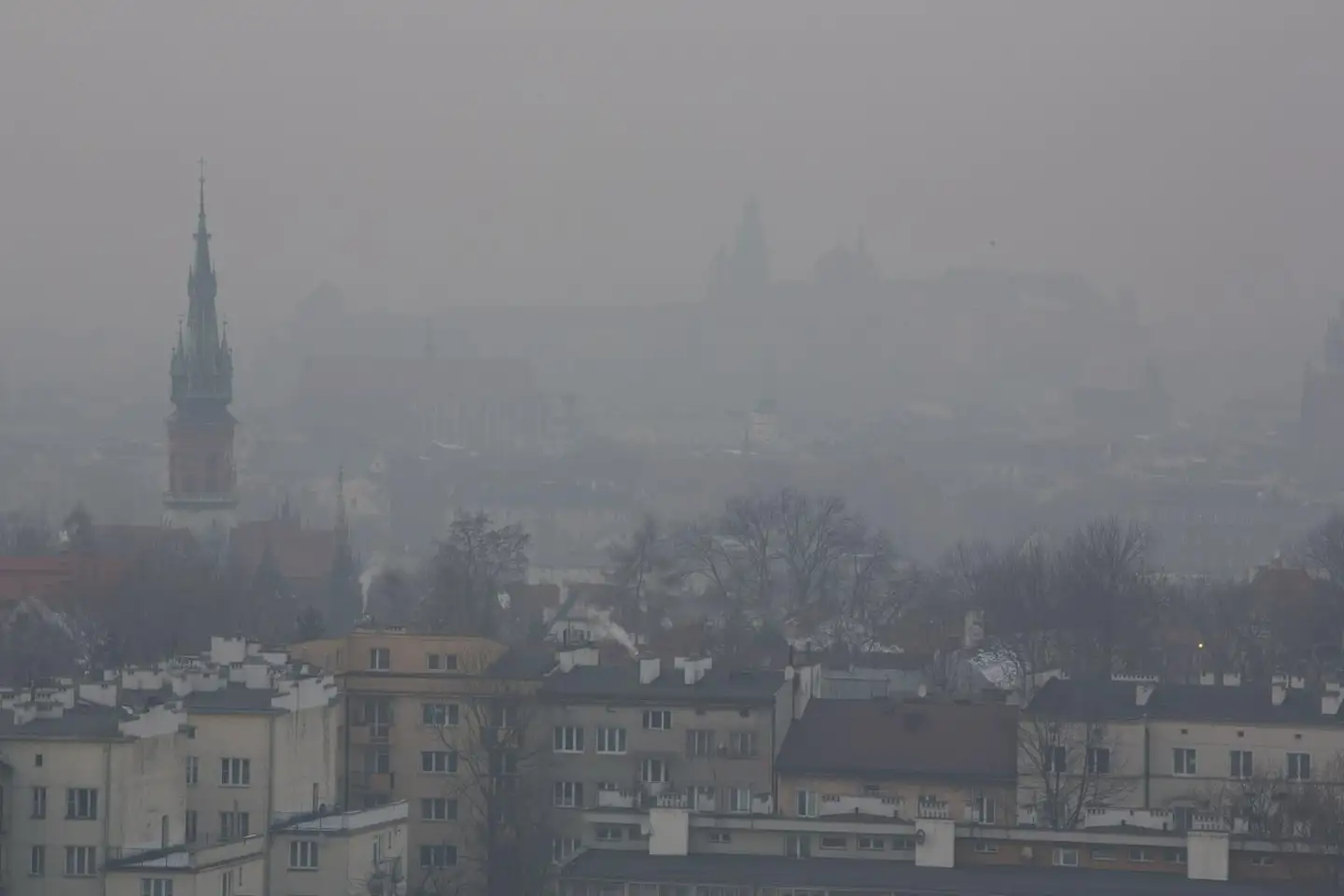 Kraków w szarym smogu, wieża kościoła ledwie widoczna nad dachami